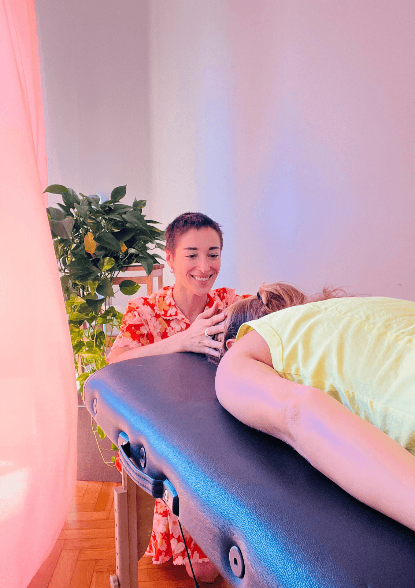 Person receiving a massage while lying on a table in a bright room next to a green plant.